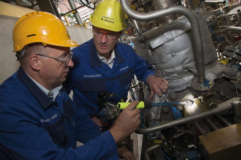 Two BASF employees inspect a sensor on a pump in an amine production plant.