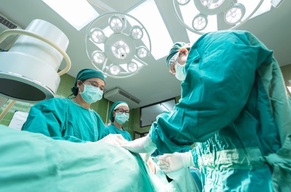 Three people in green clothes stand around an operating table.