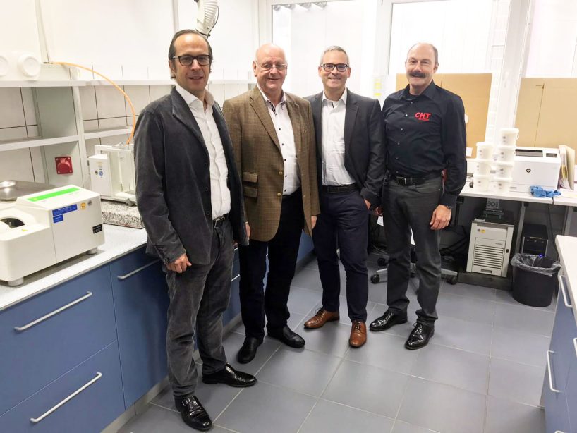 Four men in business outfits stand next to each other in a laboratory.