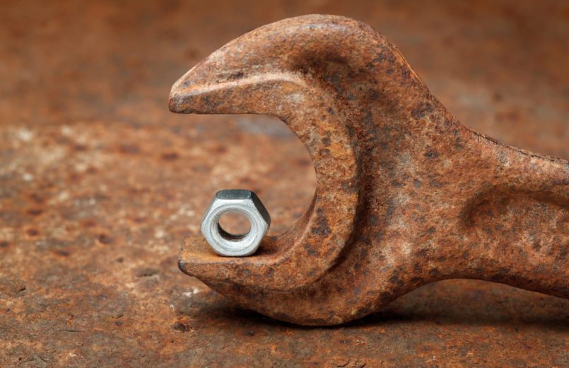 Shiny nut lies in a rusted wrench.