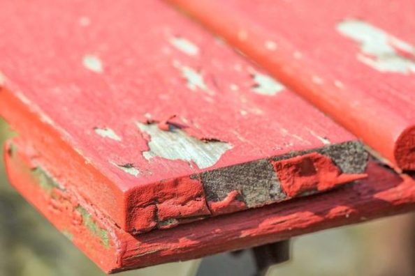 A red coating is peeling off a wooden board.