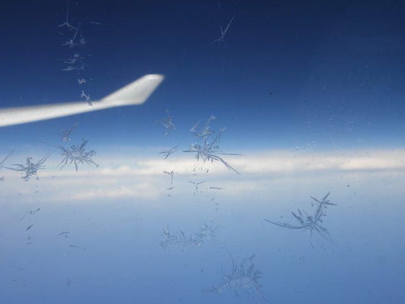 A wing seen through a partly iced up aircraft window