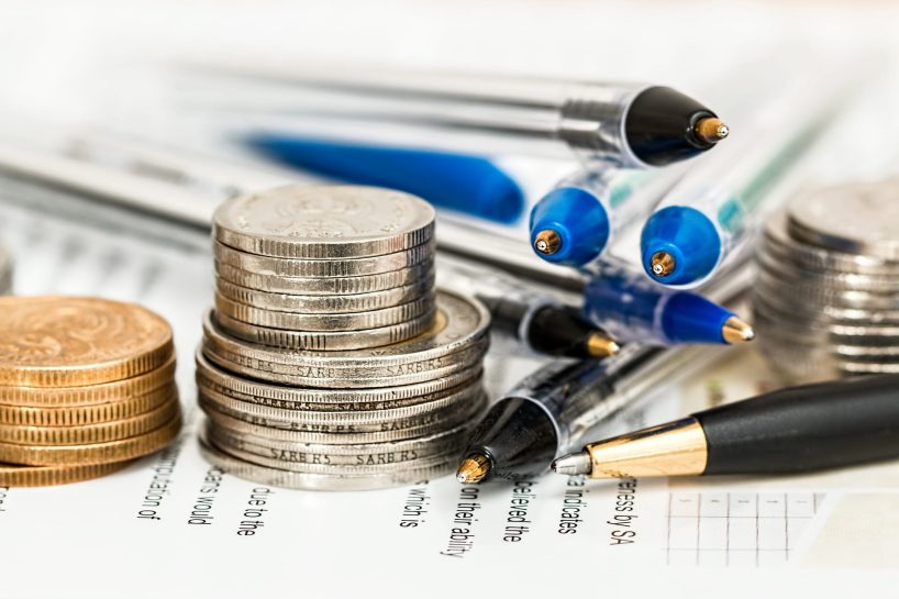 Pens and coins lie on a pile of documents.