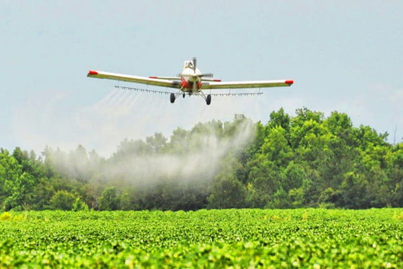 An aircraft releases fertiliser over an agricultural field in low-level flight.