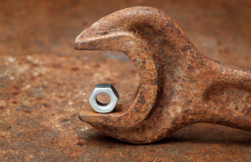 A nut lies on a rusted wrench.