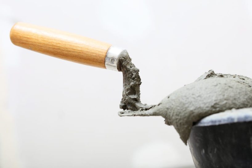 A trowel with grey paste lies on the edge of a bucket.