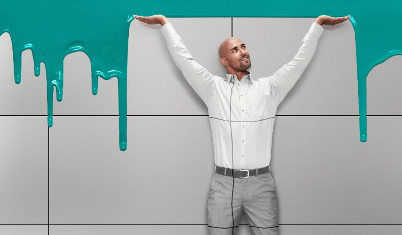 A man stands with his hands raised in front of a tiled wall