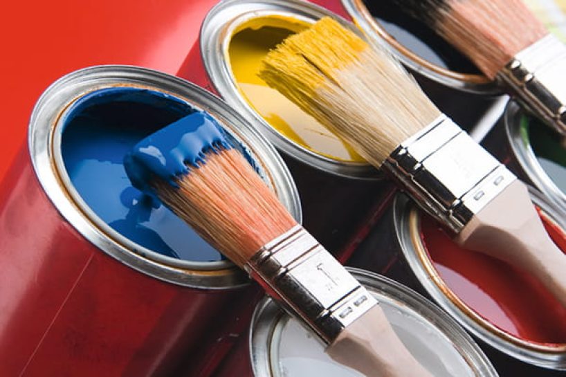 Several cans of lacquer of different colours with brushes lying on top.