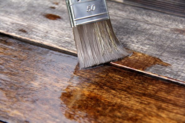 A brush is used to apply transparent liquid to wood.