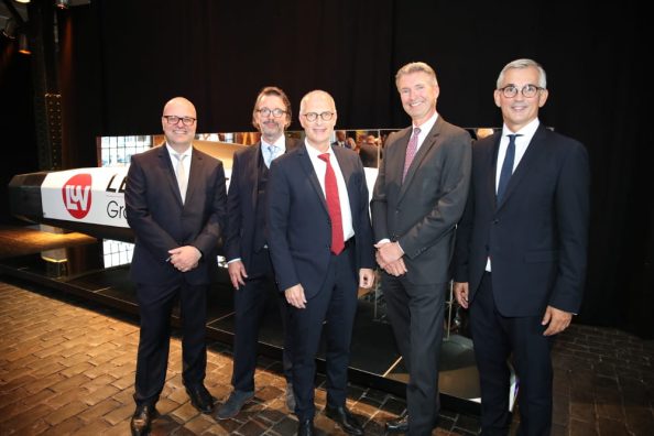 Five men in a suit and tie stand next to each other in front of a black