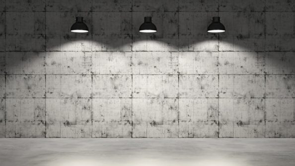 Three black ceiling lamps in front of a grey concrete wall and grey floor.