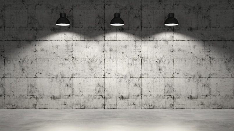 Three black ceiling lamps in front of a grey concrete wall and grey floor.