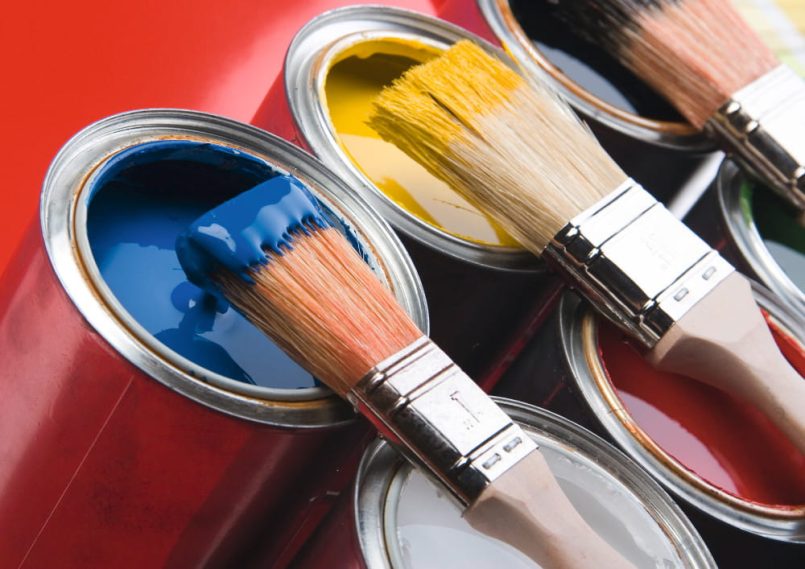 Brushes dipped in paint lie on open paint cans.