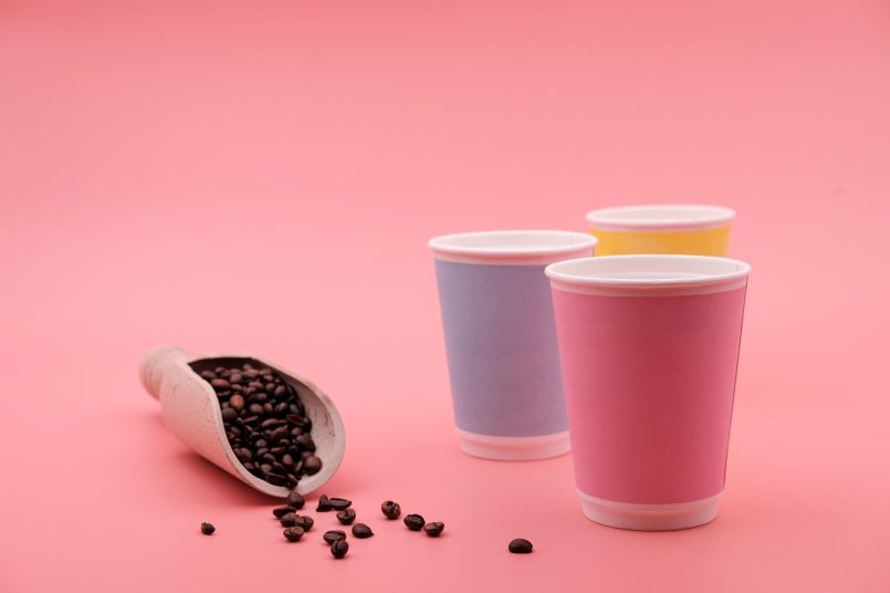 Three colorful paper cups next to a shovel with coffee beans.