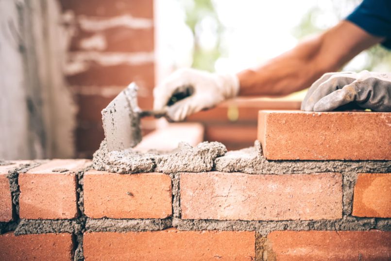 Hand with trowel and mortar on a brick wall.