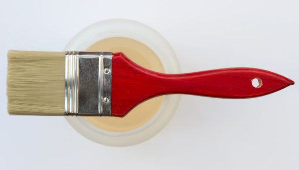 Red brush lies on a round container with light liquid.