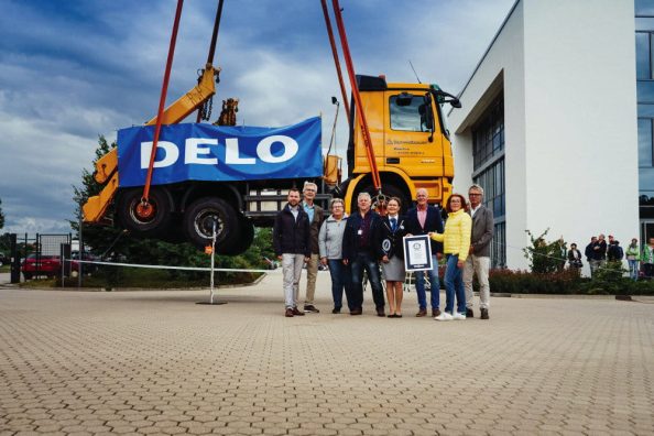 Men and women with a certificate in front of a truck hanging on ropes in the air.