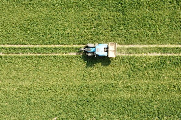 A tractor with fertiliser hopper from a bird's eye view on a field.