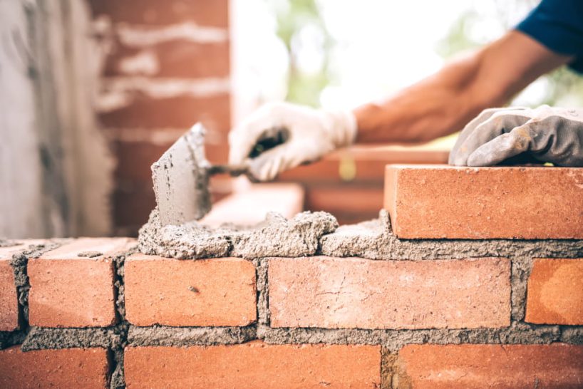 Hand passes with a spatula mortar on a brick wall.