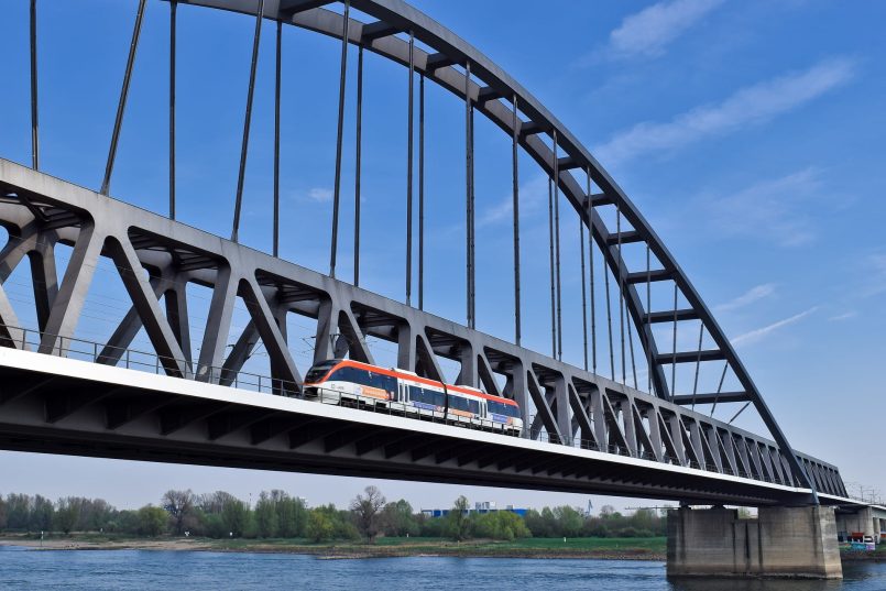 Red light railway crosses a railway bridge over a river.