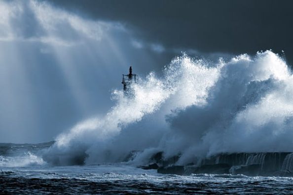 A very large wave hits a lighthouse in stormy weather.