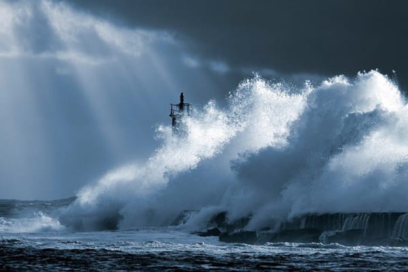 A very large wave hits a lighthouse in stormy weather.